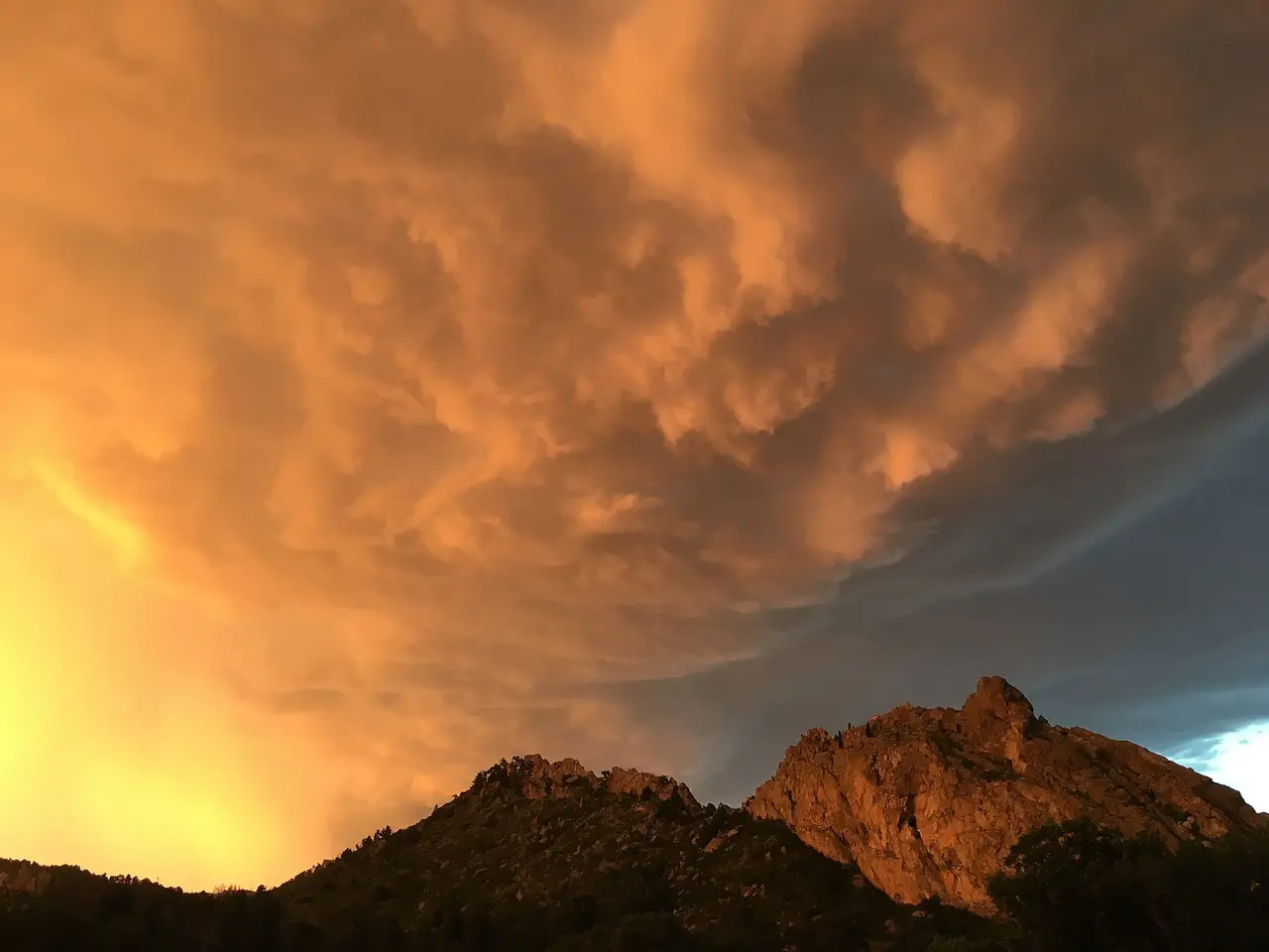 Orange sunset clouds above dark red rock formations