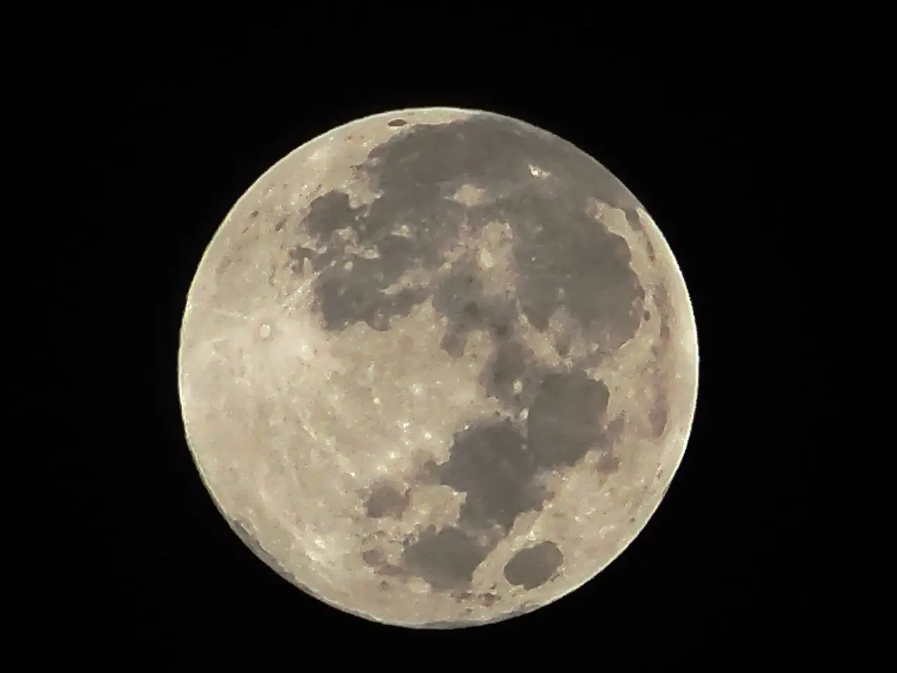 A full moon with grey patches on a black sky