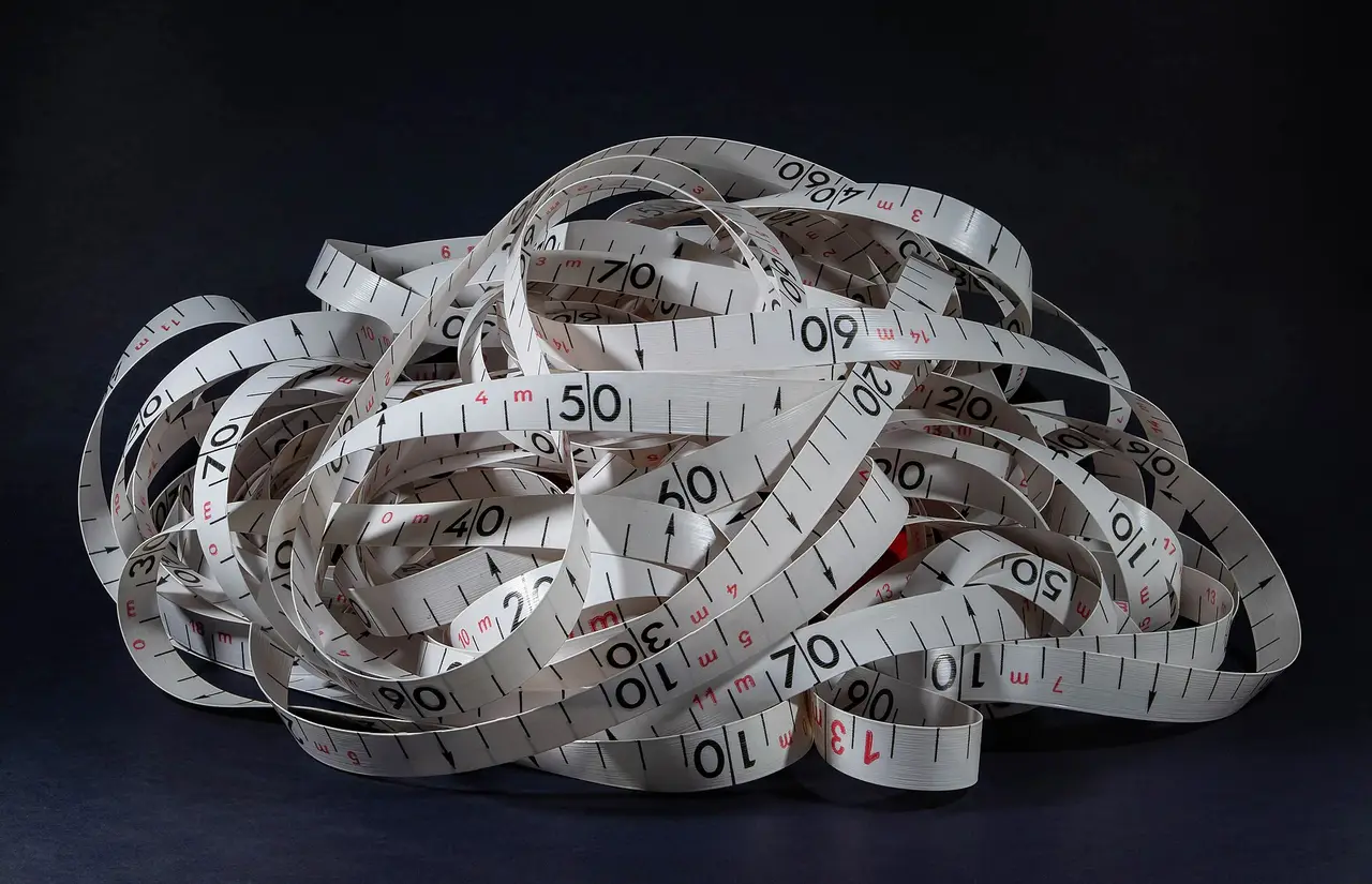 A pile of loose white measuring tape with black numbers on a dark background