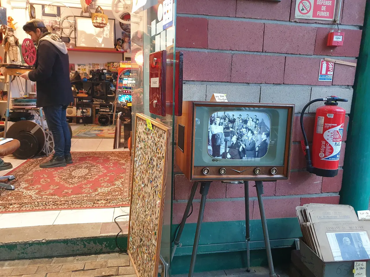 A small old television on a stand beside a fire extinguisher