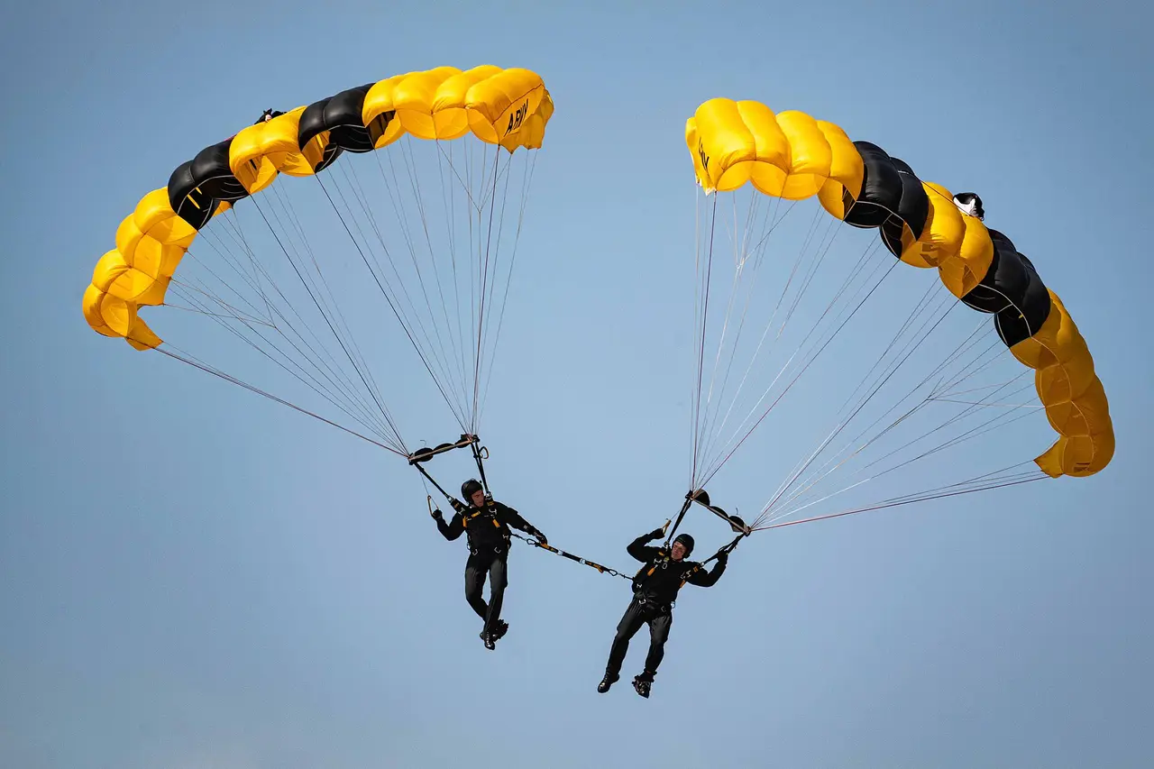 Two skydivers under yellow and black parachutes in a blue sky