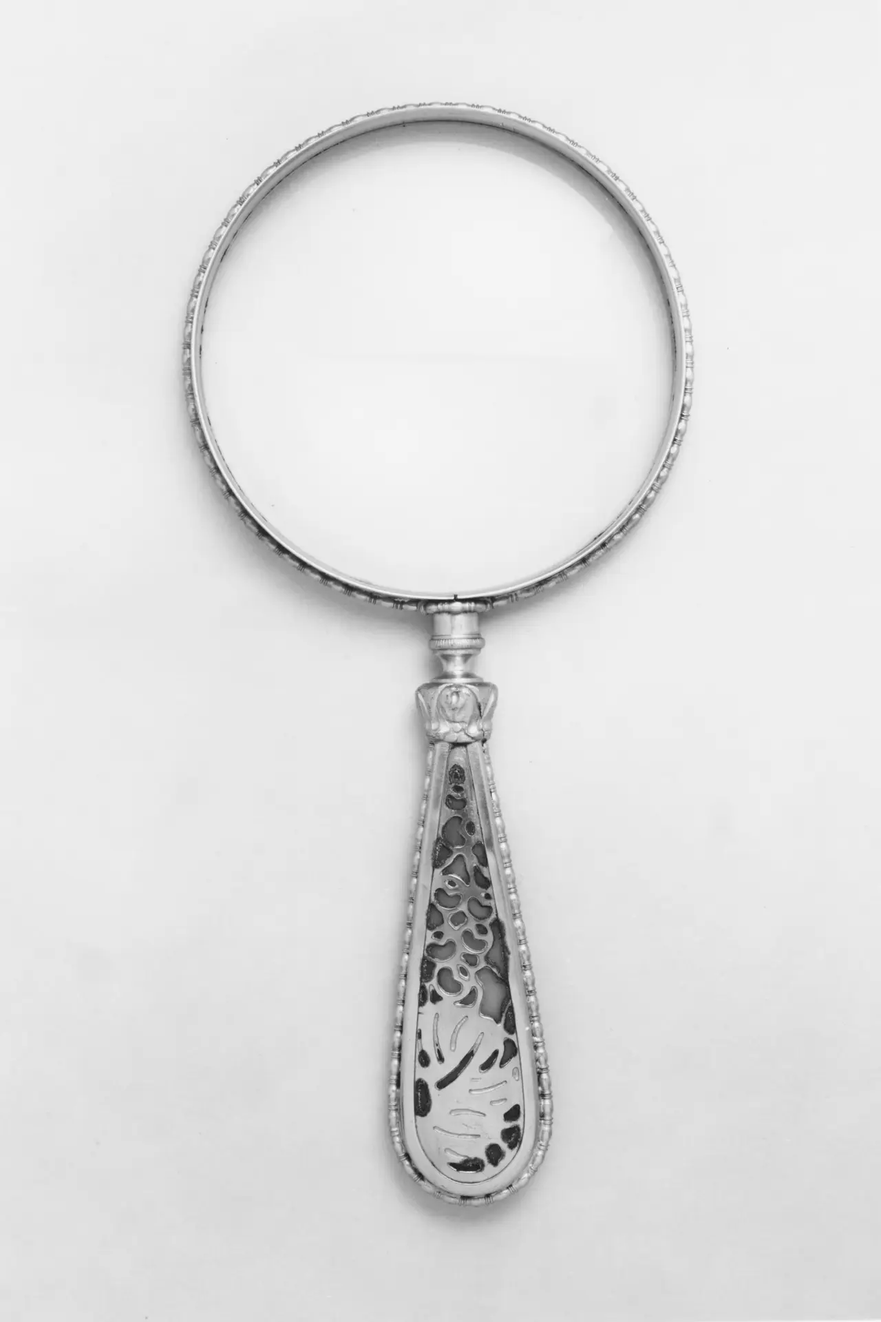 A magnifying glass with a patterned silver handle on white