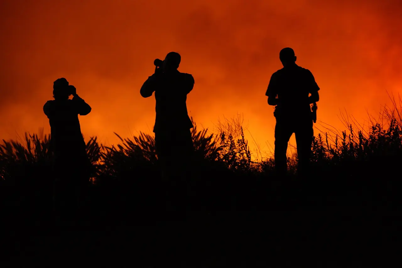Three dark silhouettes standing against glowing orange flames