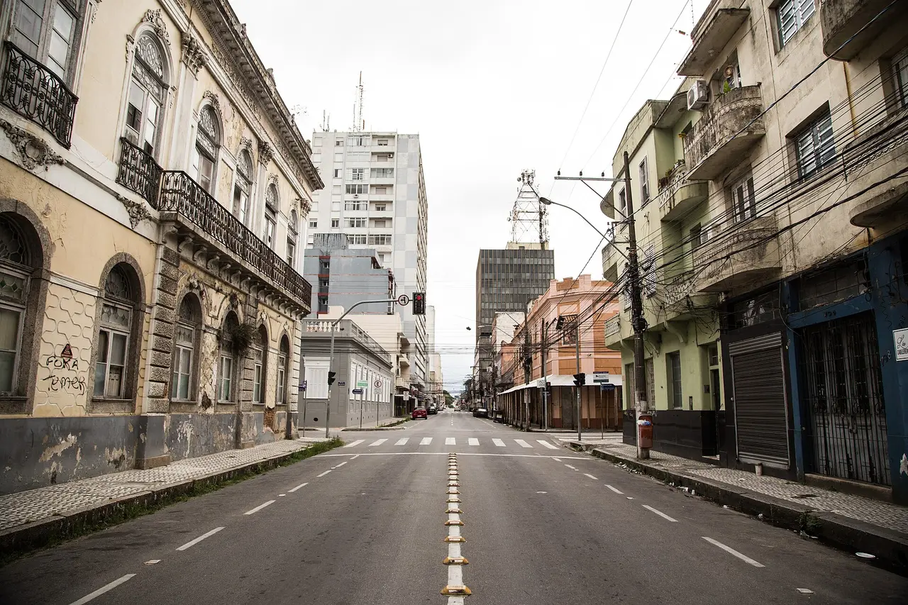 An empty city street between old buildings under a cloudy sky