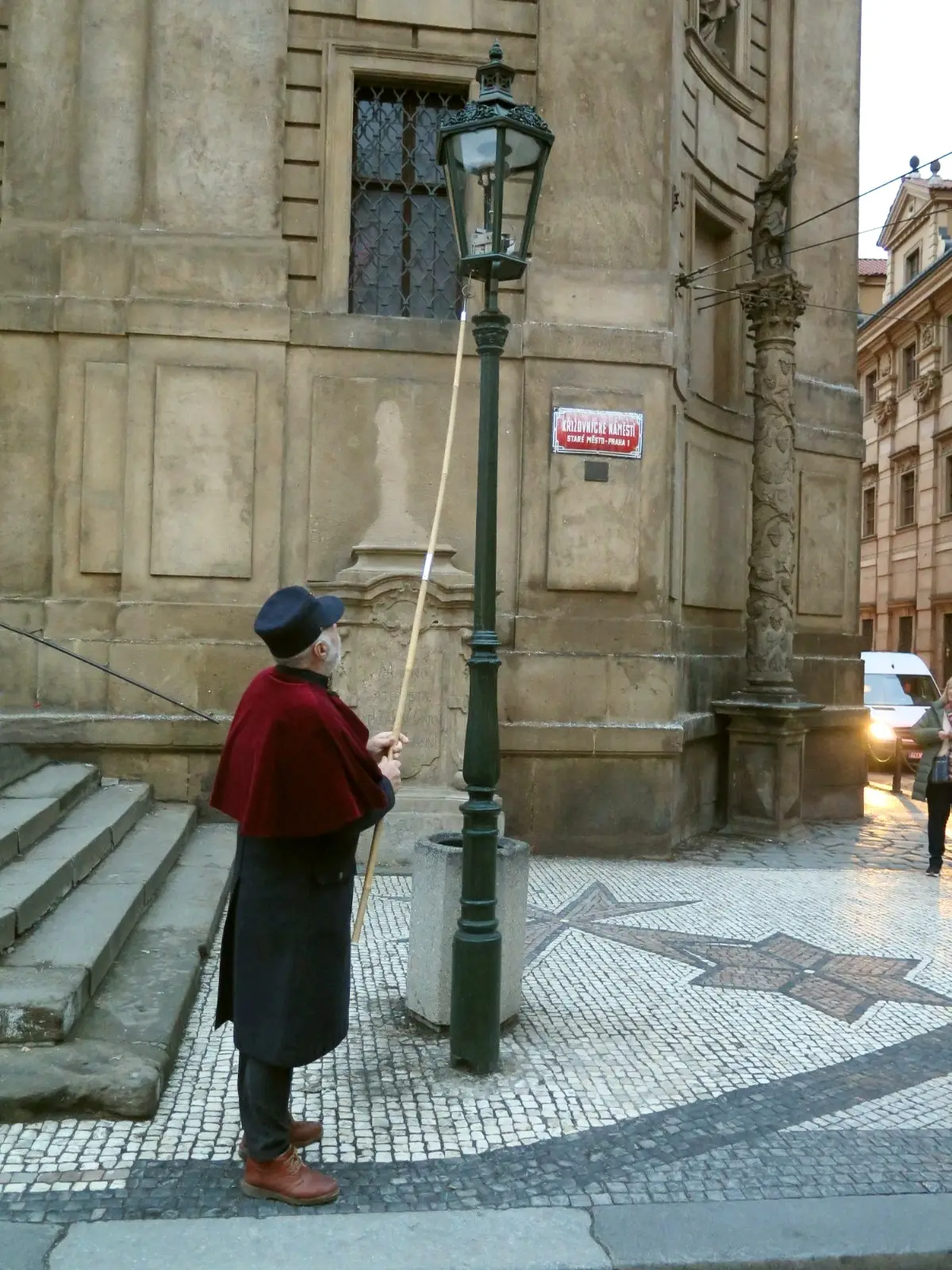A man in a red cape holding a pole beside a street lamp