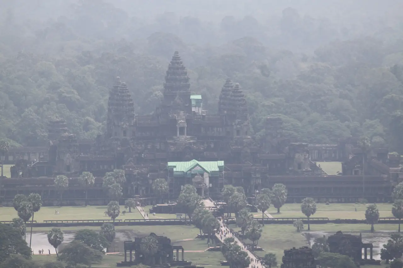 Aerial view of Angkor Wat's towers and causeway among trees in haze