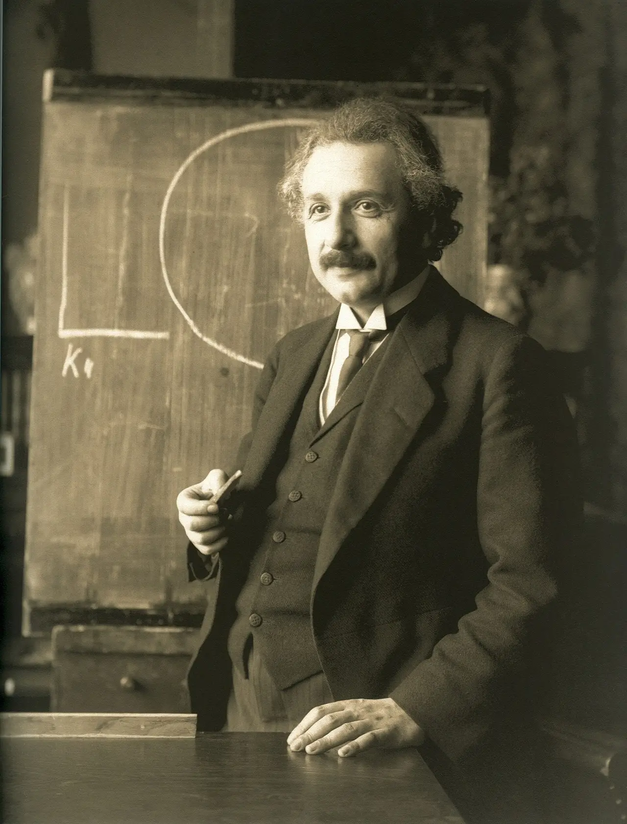 A man in a suit standing in front of a blackboard