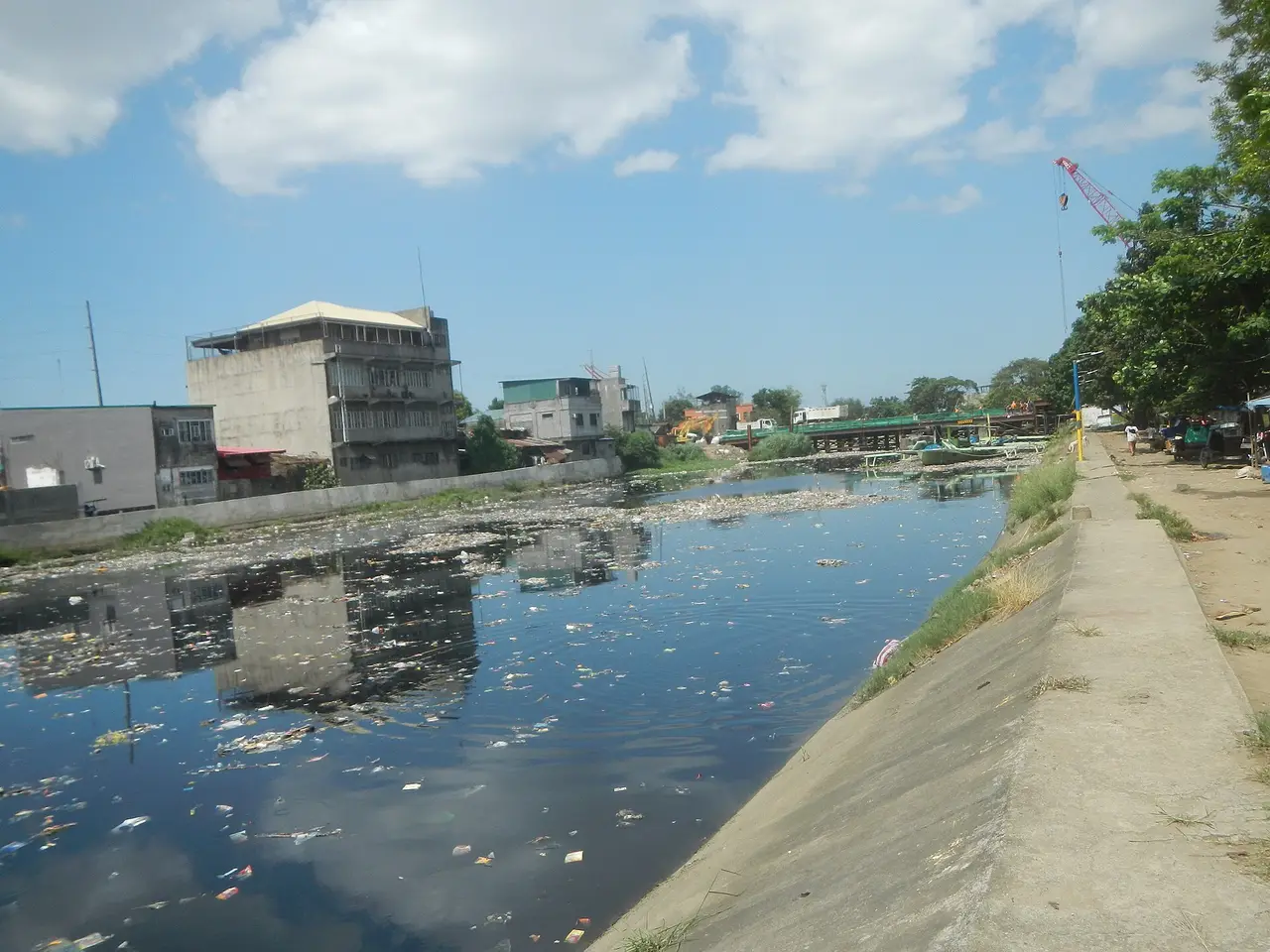 A river with floating rubbish beside a concrete embankment
