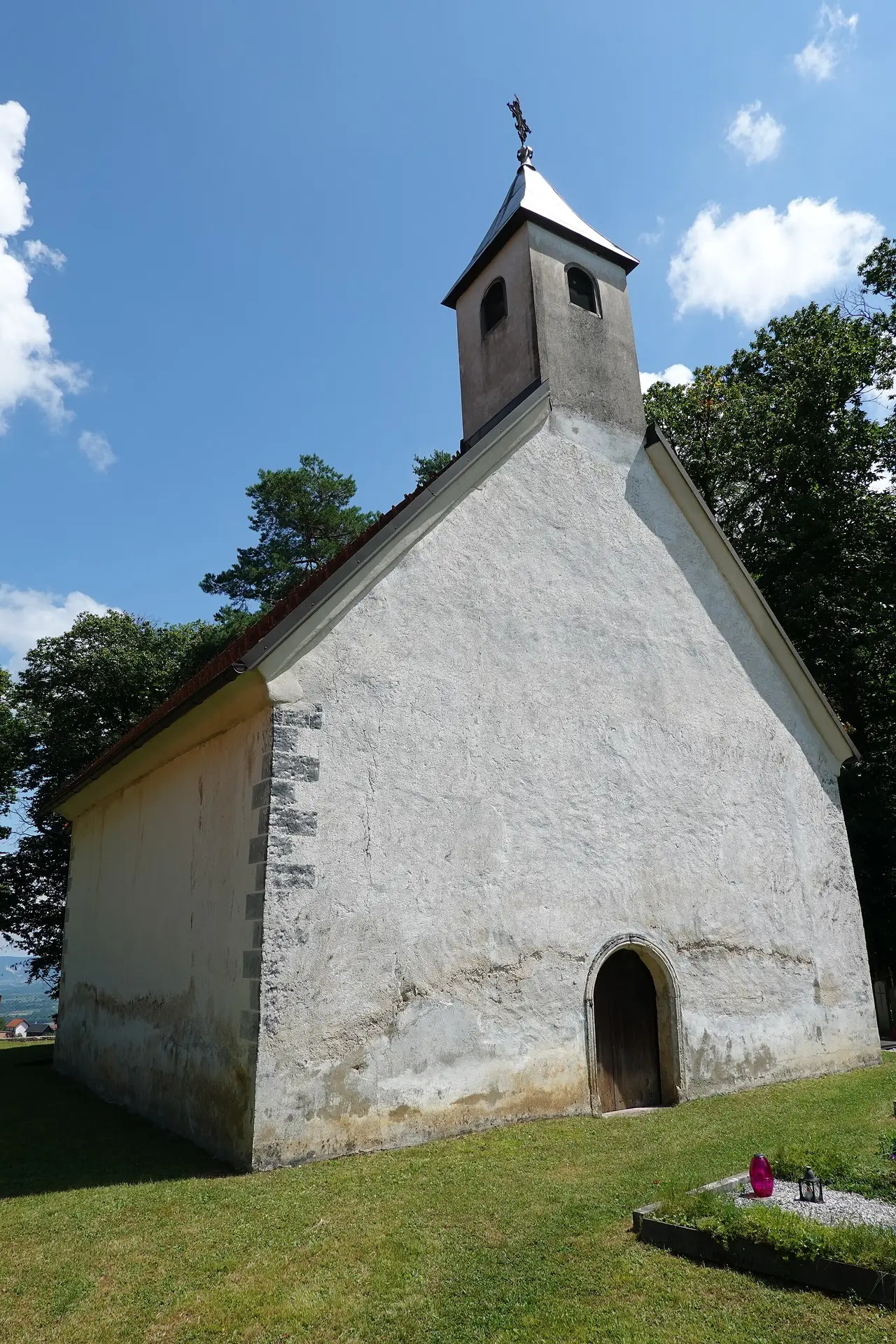 A white church with a red tiled roof and bell tower on a grassy slope