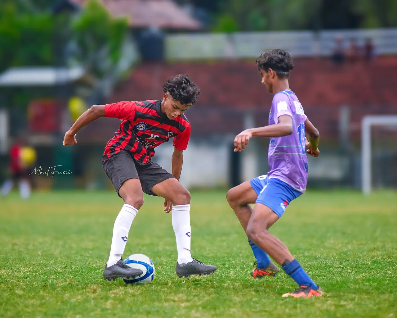 Two young footballers challenge for the ball on a grass pitch