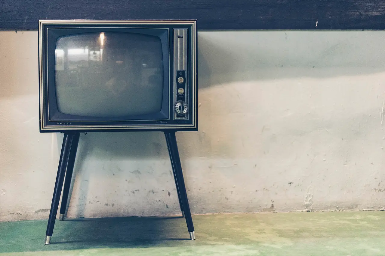 An old television on tall thin legs in front of a pale wall
