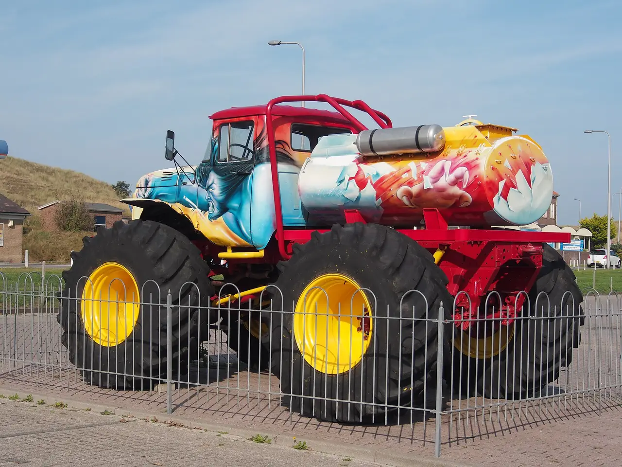 Large painted monster truck on yellow wheels behind a low fence