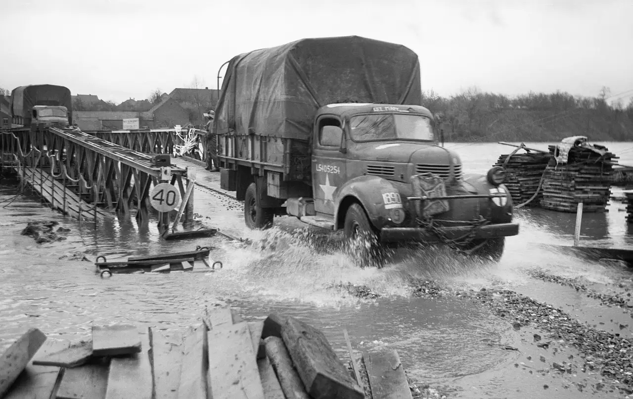 A covered lorry driving across a flooded Bailey bridge in 1944