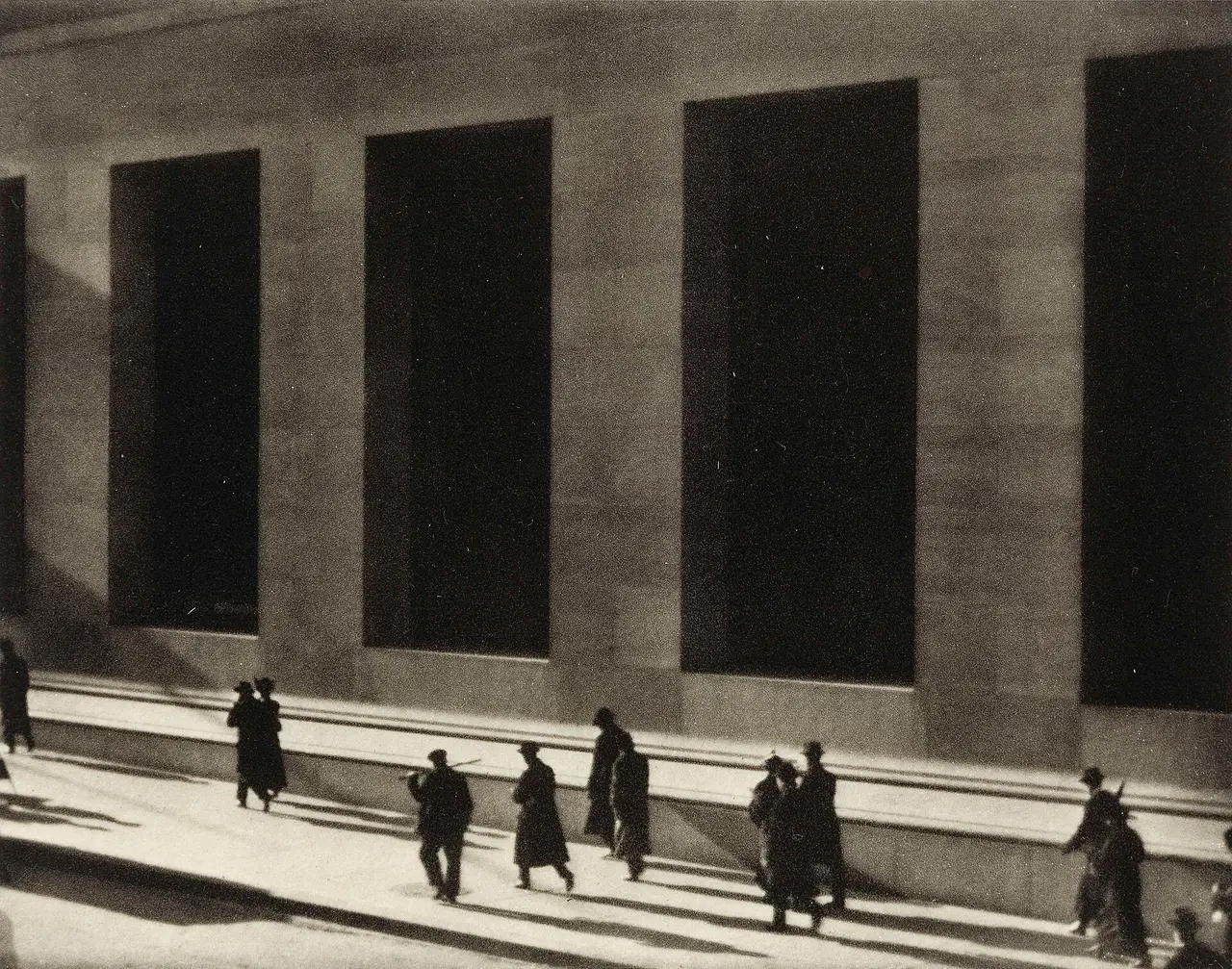 Black and white photograph of people walking below tall windows on Wall Street