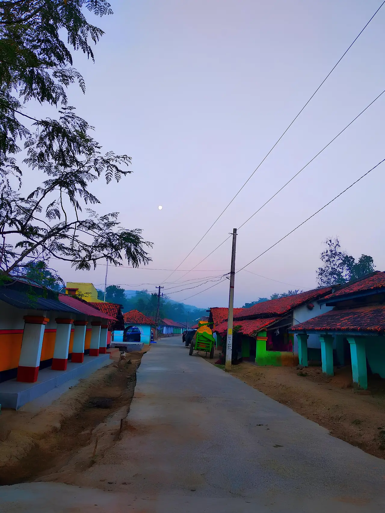 A village road with power lines and small coloured houses at dusk