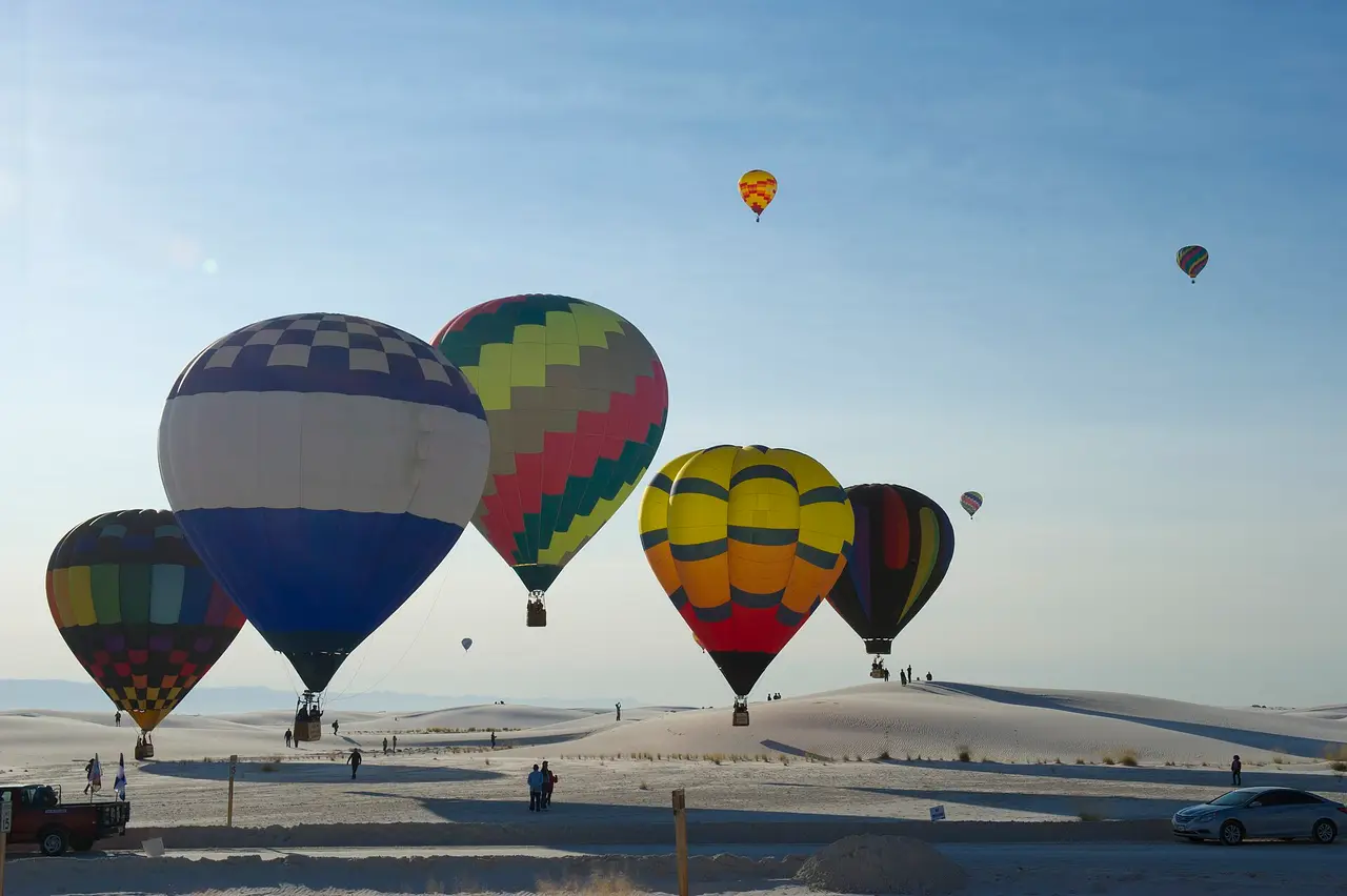 Colourful hot air balloons above pale desert dunes under a clear sky