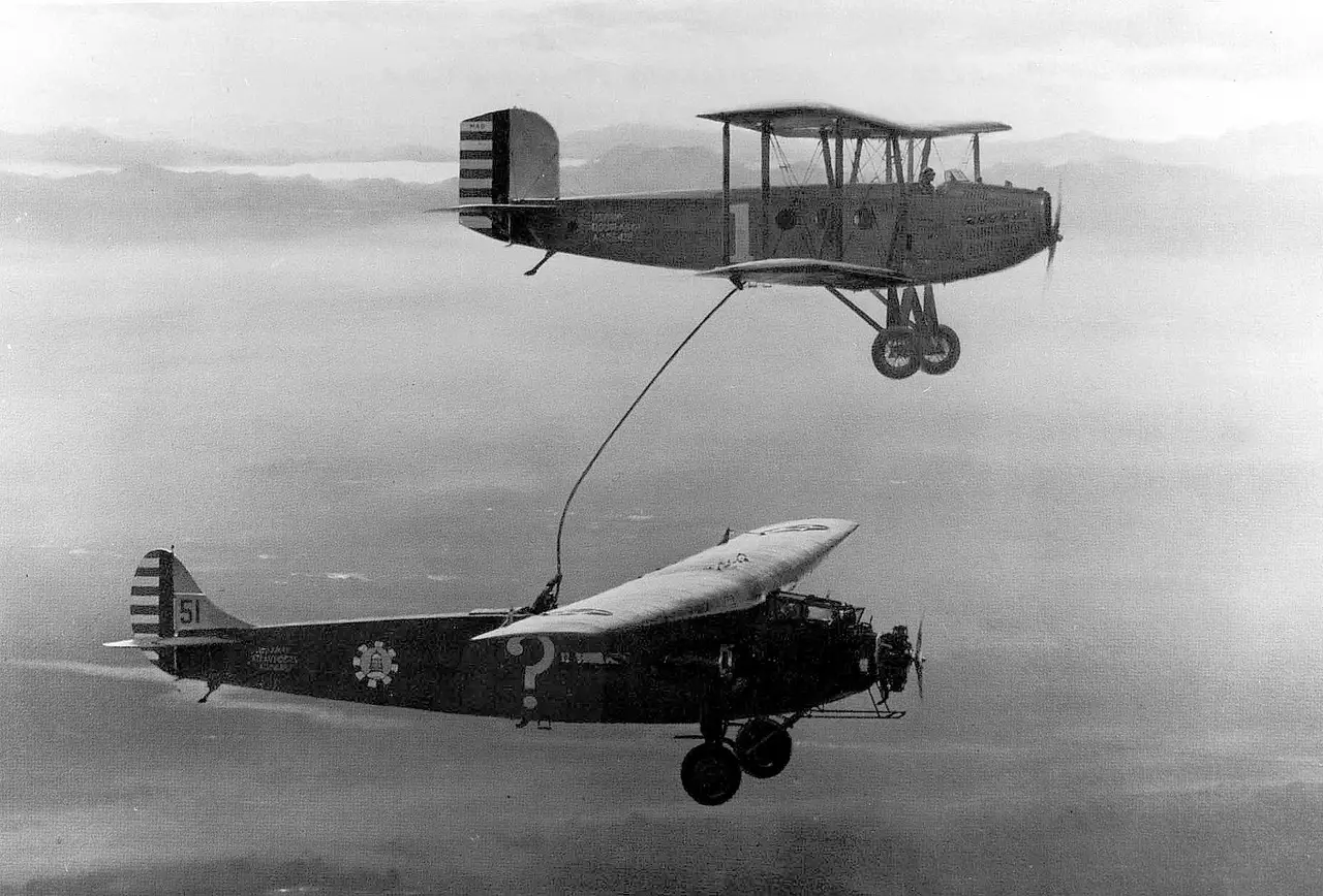 Black and white photo of a biplane refuelling a monoplane in flight