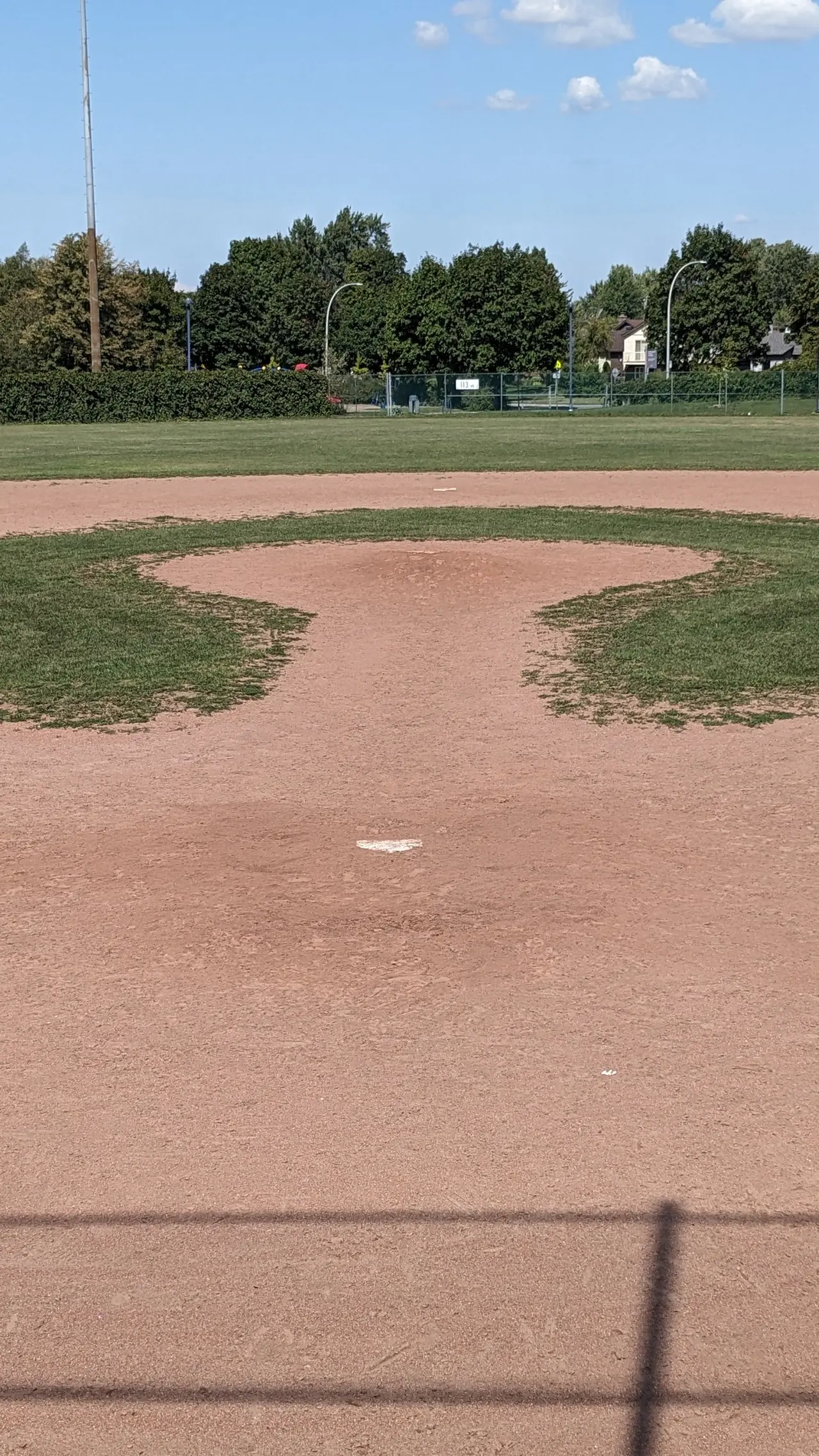 Dirt pitcher's mound on an empty baseball field with trees behind