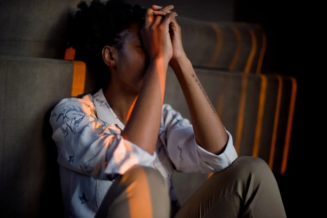 A woman seated with her hands over her face and head