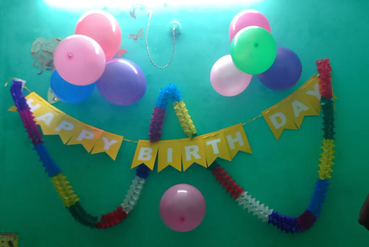 A Happy Birthday banner and balloons on a green wall