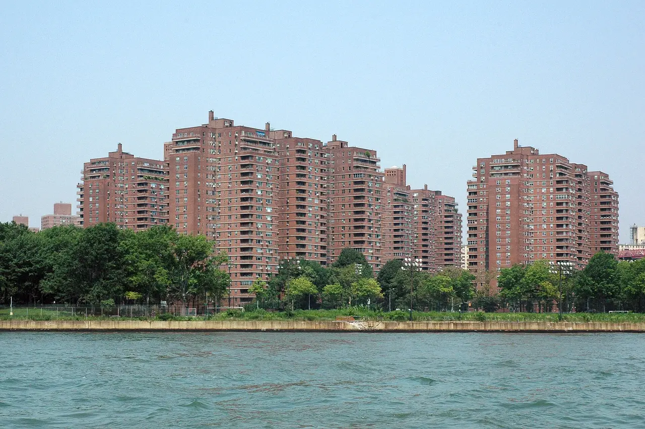 Brick apartment towers behind trees on the shore of a river