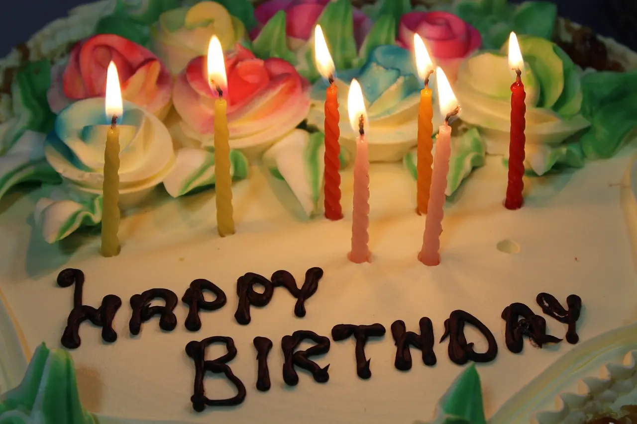 Birthday cake with icing roses, Happy Birthday lettering and seven lit candles