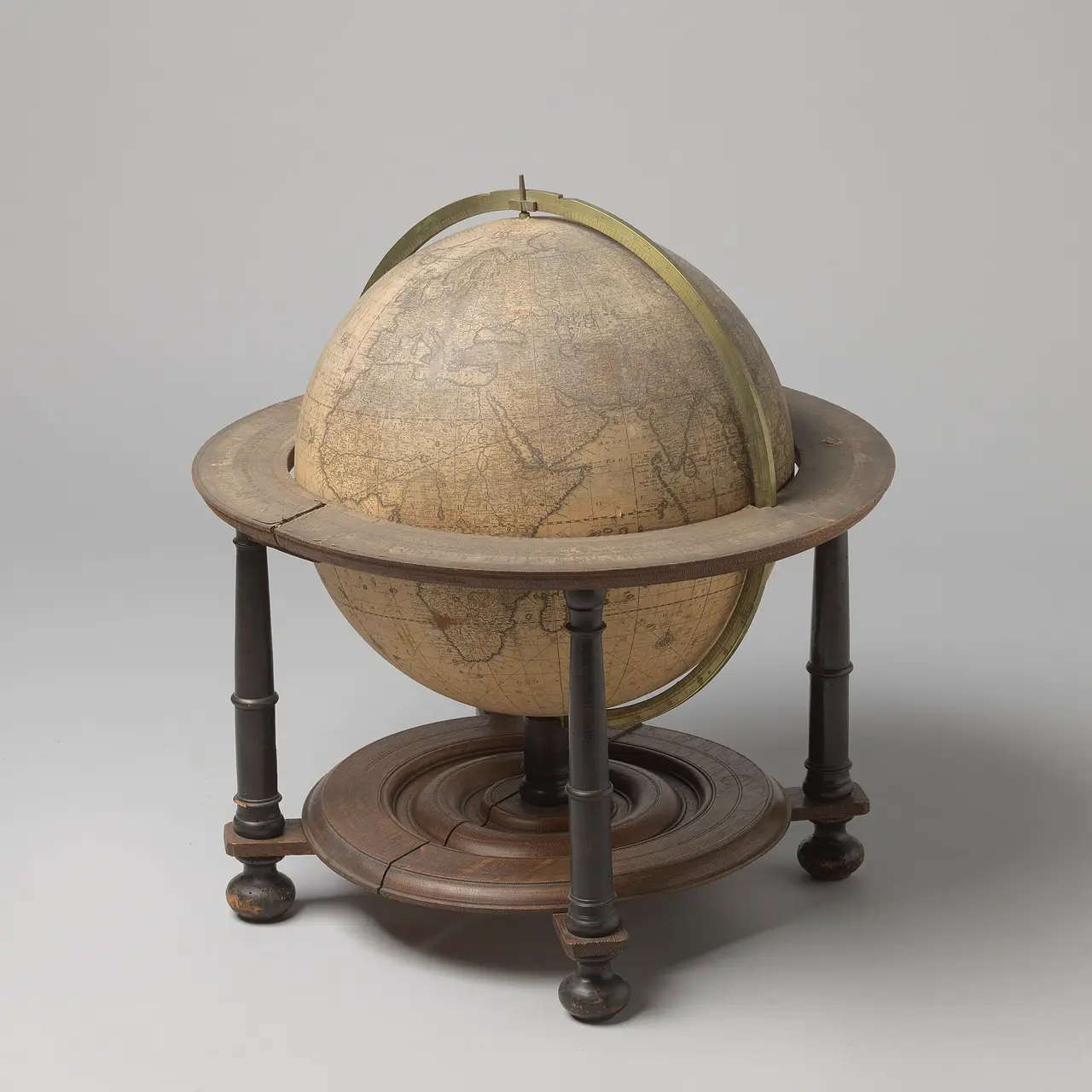 An old terrestrial globe held in a round wooden stand on four legs