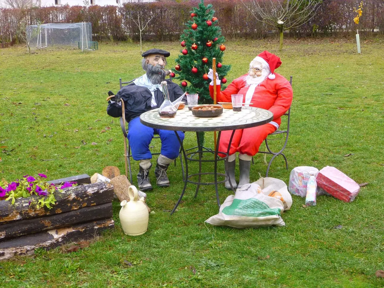 Santa Claus and Olentzero figures seated at a garden table with a Christmas tree