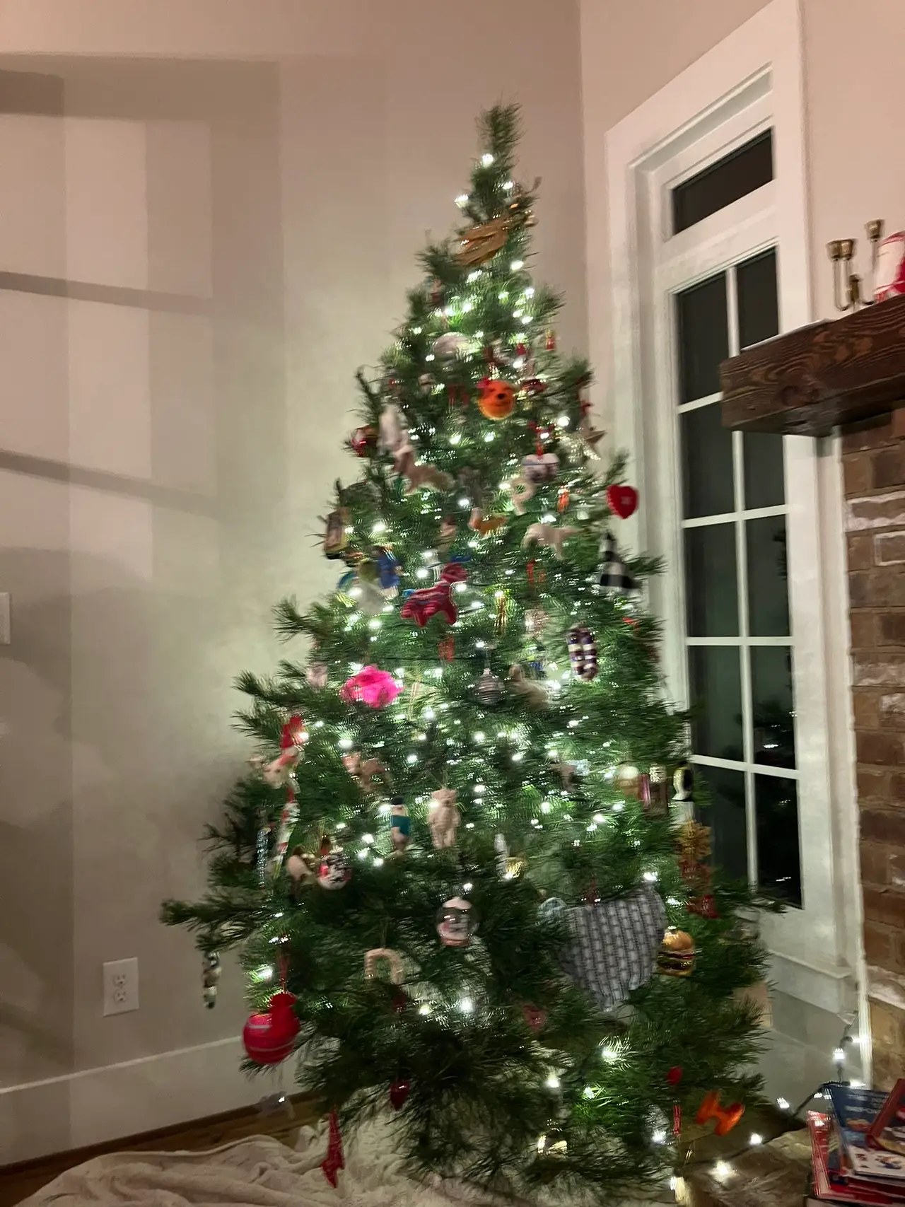A lit Christmas tree with red and pink baubles in the corner of a room