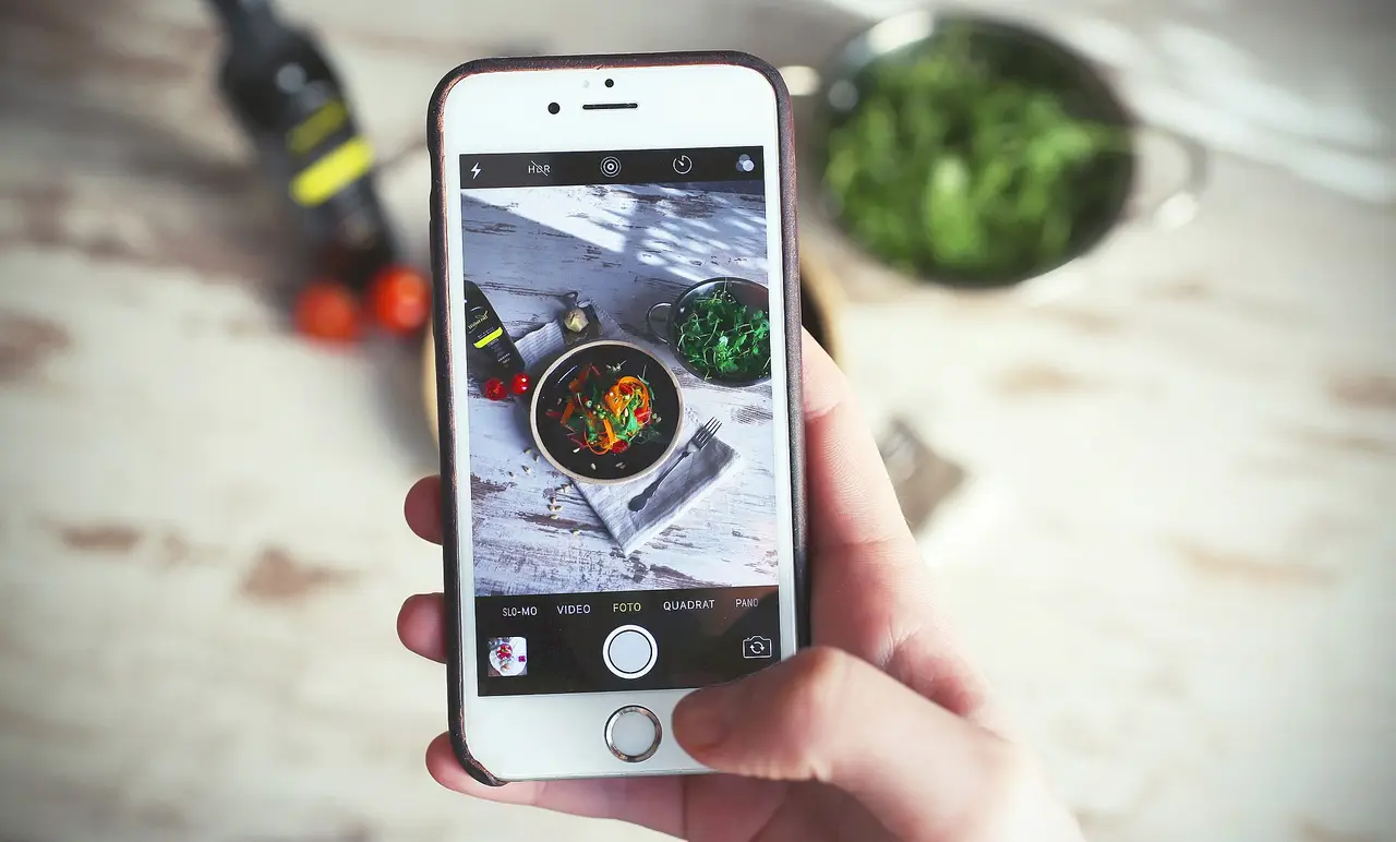 A hand holding a smartphone to take a photo of a bowl of food