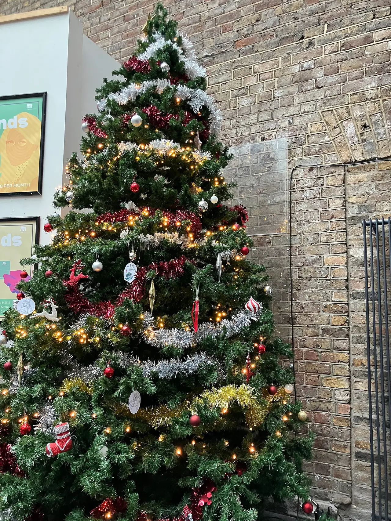 A tall decorated Christmas tree standing against a brick wall