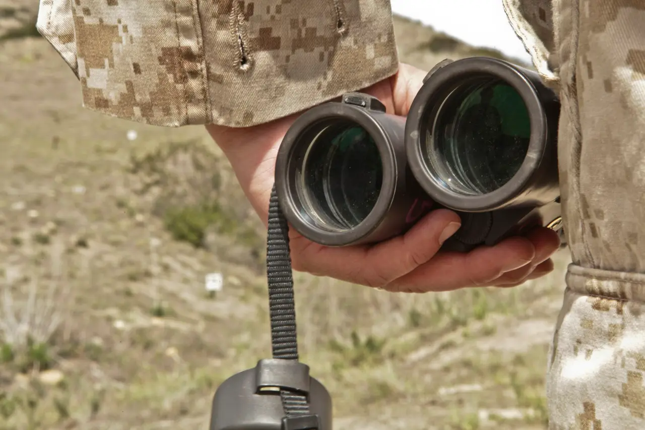 Hands holding black binoculars beside a camouflage uniform