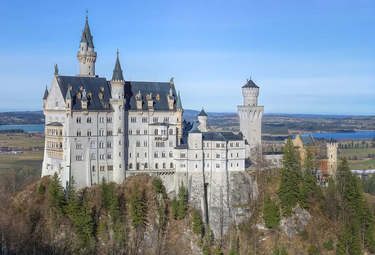 White towered castle on a wooded hill under a blue sky