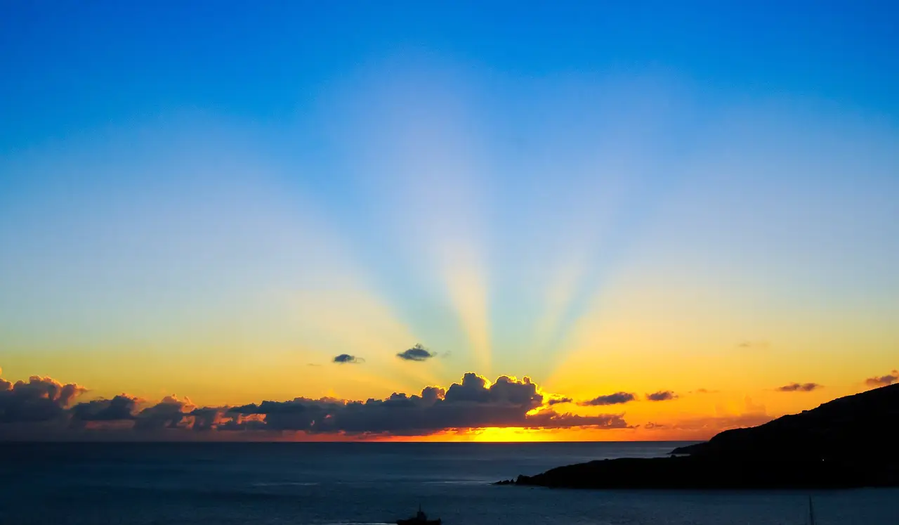 Orange and yellow sunset with rays of light over a dark sea