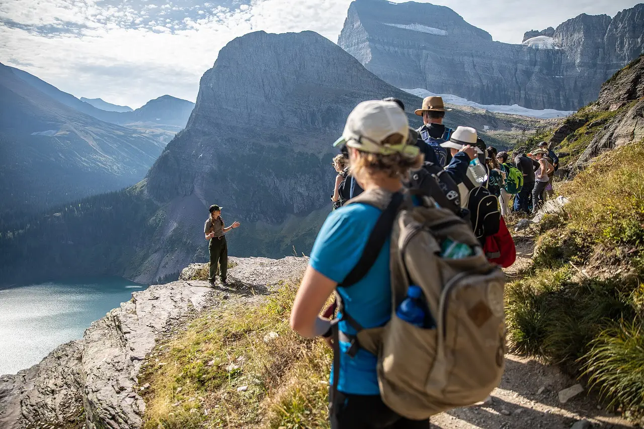 Hikers with backpacks gathered around a park ranger on a mountainside above a valley