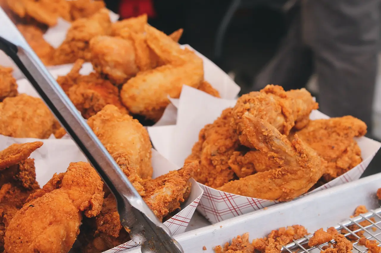 Crisp fried chicken pieces in paper trays with tongs