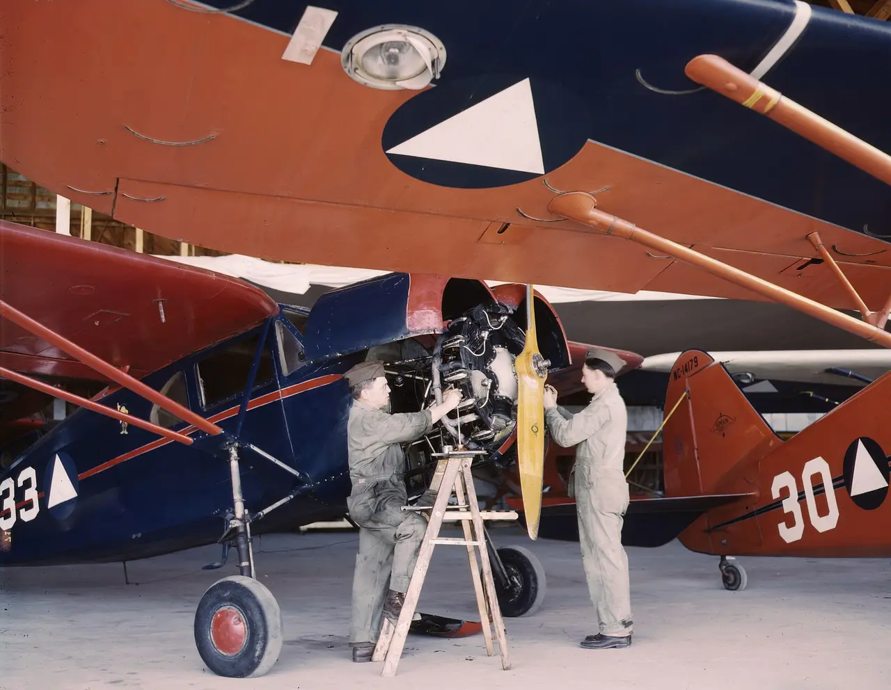Two mechanics beside red and blue Civil Air Patrol aircraft in a hangar