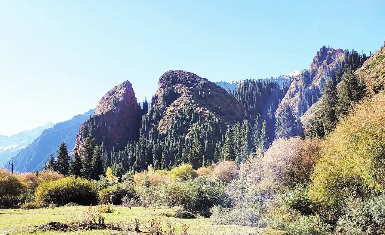 Two red rock formations split like a broken heart above trees and mountains
