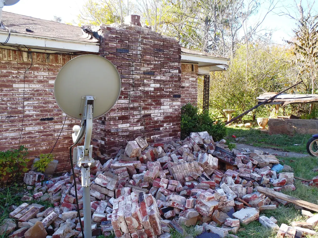 A pile of fallen bricks beside a house with a satellite dish