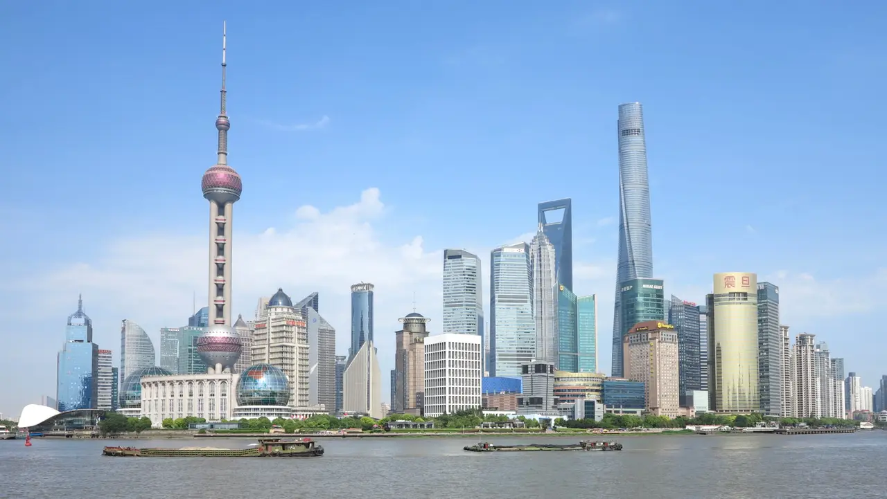 The Pudong skyline across a river under a blue sky