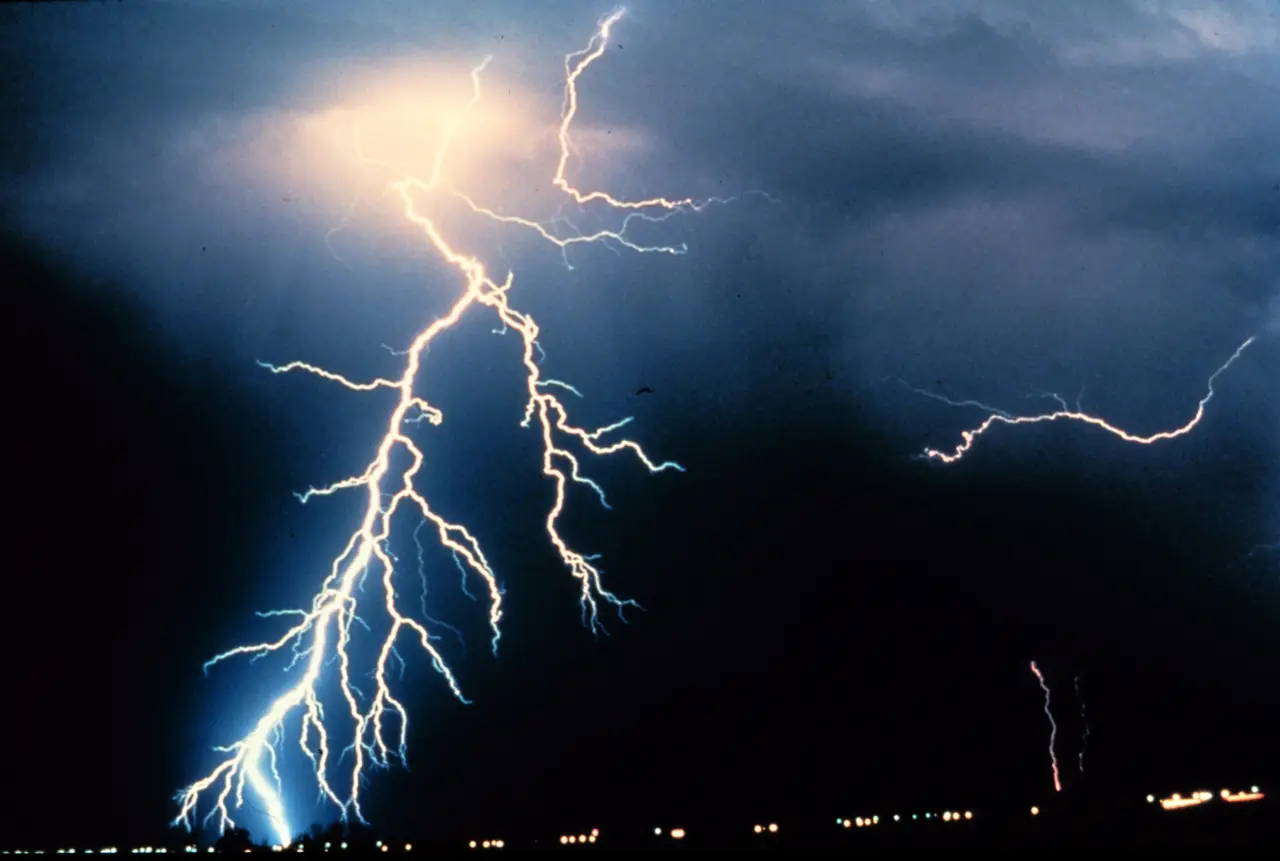 Forked lightning against a dark stormy sky above distant lights