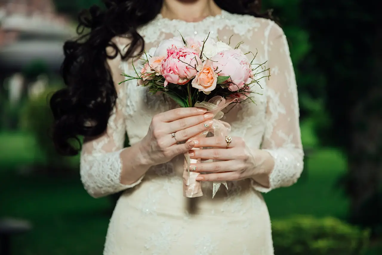 A bride in a lace dress holding a pink rose bouquet