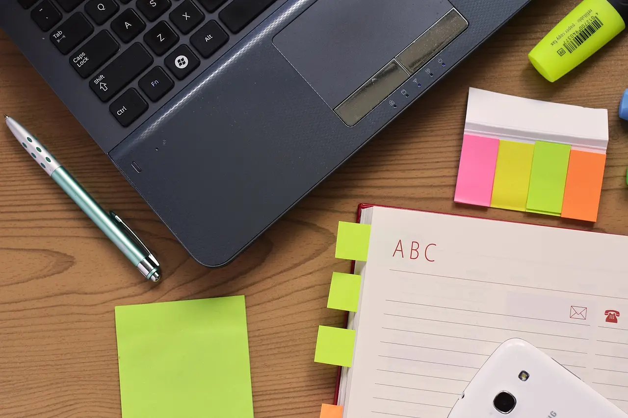 An open notebook, pen, laptop and phone lying on a wooden desk
