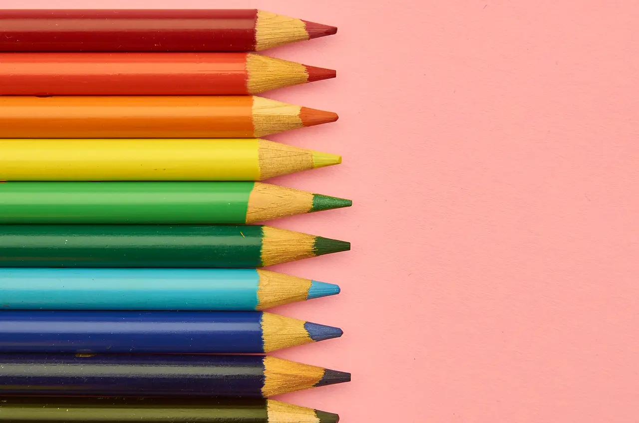 Coloured pencils lined up in a row on a pink surface