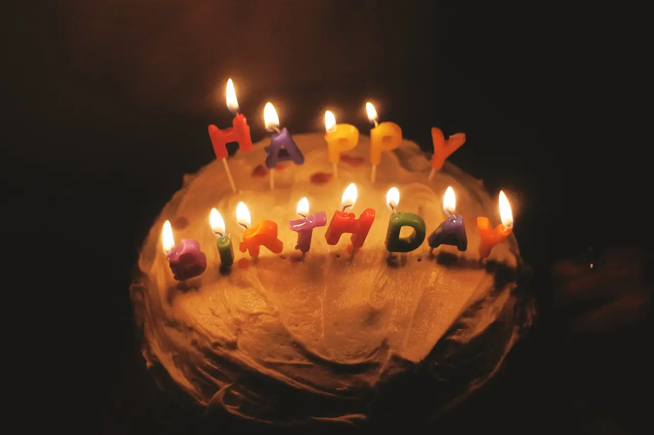 A cake topped with lit candles spelling Happy Birthday in a dark room