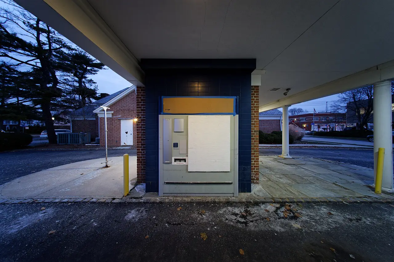 A drive-through lane under a canopy with a teller machine at dusk