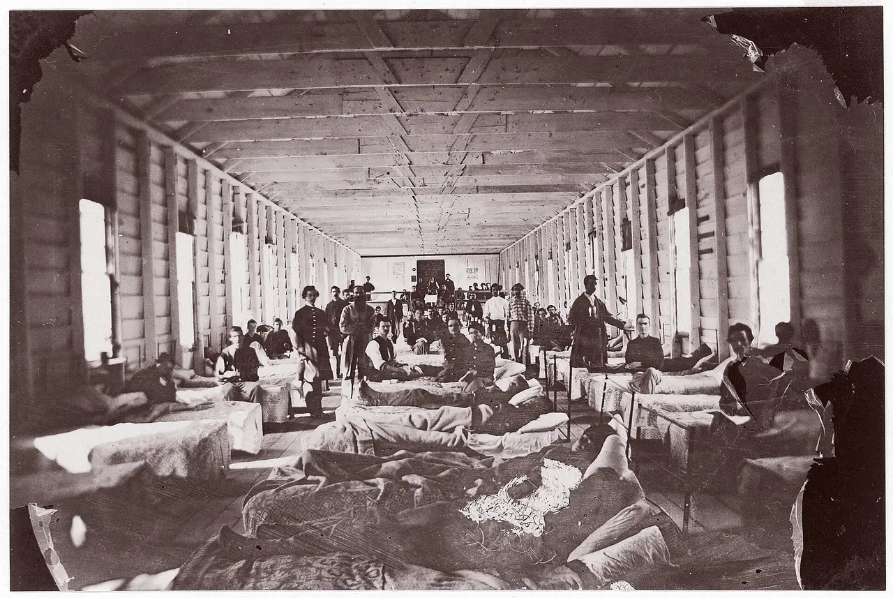 A long hospital ward with rows of beds and people in the central aisle