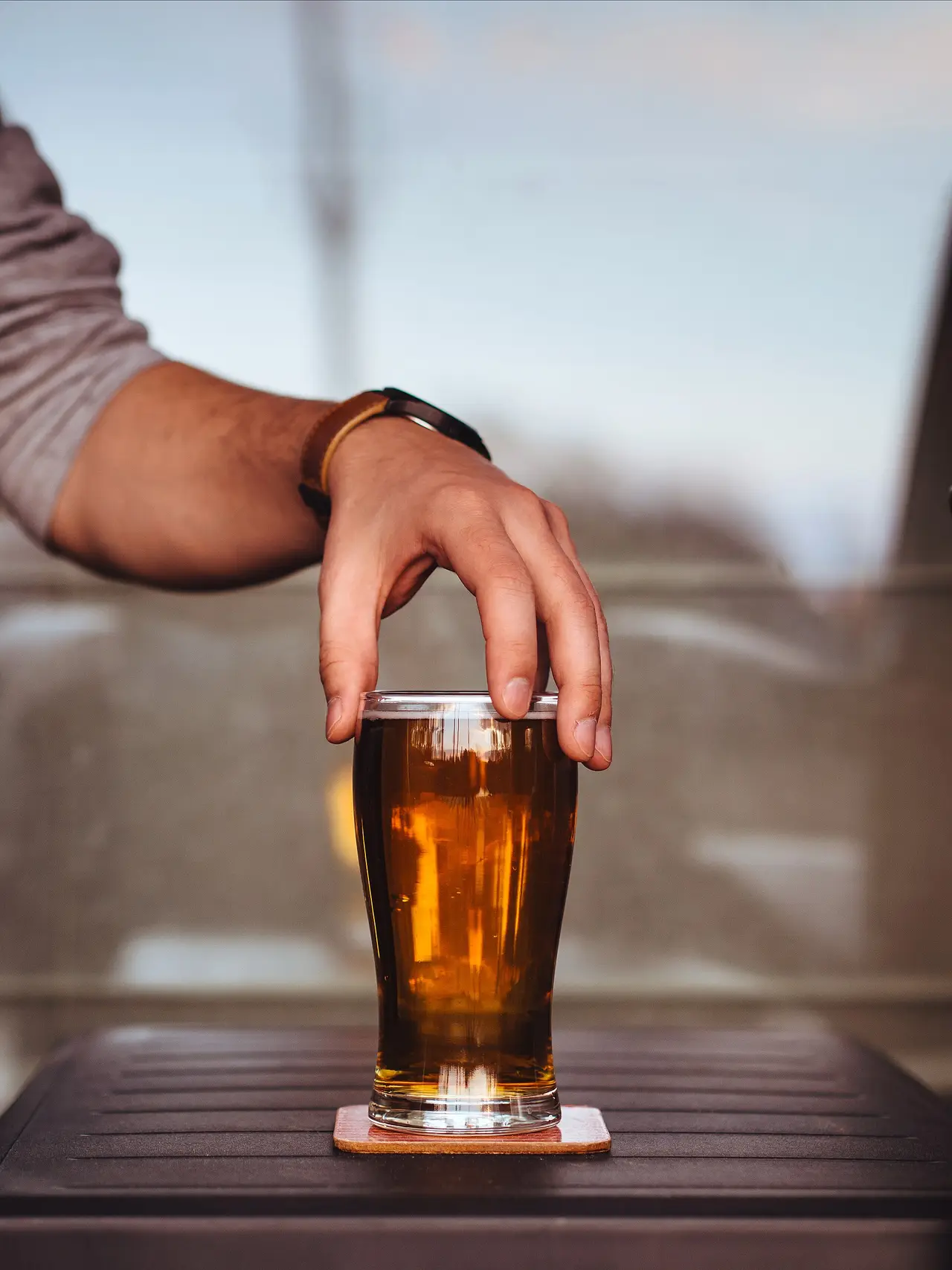 A hand holding a glass of amber beer on a table