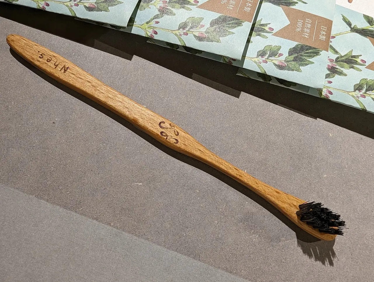A wooden toothbrush with dark bristles lying on a grey surface