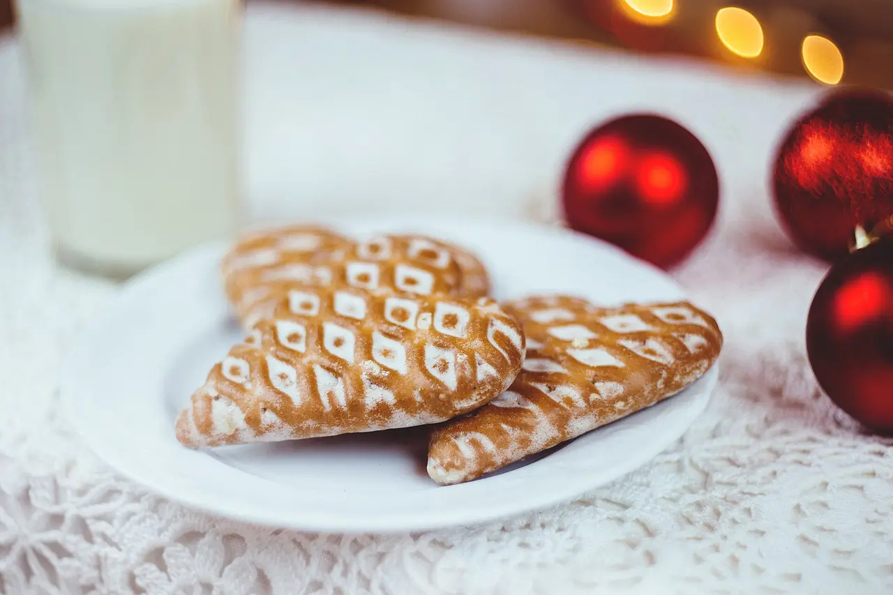 Lattice-iced gingerbread cookies on a plate next to a glass of milk and red baubles